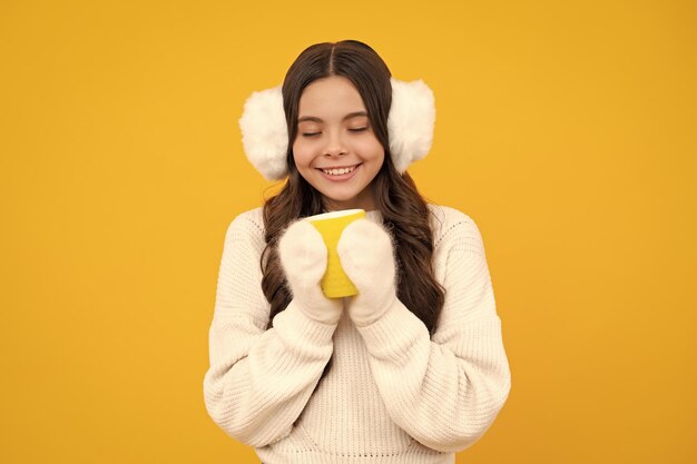 Foto chica adolescente en invierno orejeras cálidas y suéter con una taza para llevar de café capuchino o té niño con una taza de plástico para llevar bebida de cacao por la mañana