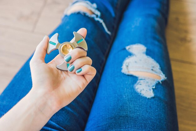 Chica adolescente en jeans agujereados sostiene en las manos y juega con spinner