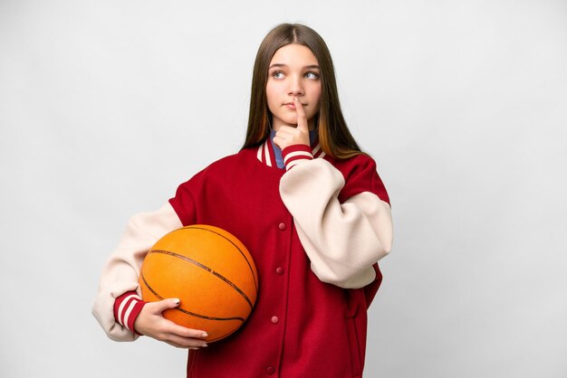 Chica adolescente jugando baloncesto sobre fondo blanco aislado que tiene dudas mientras mira hacia arriba