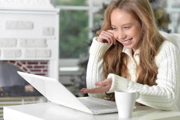 Foto chica adolescente con laptop sentada en la mesa y bebiendo té