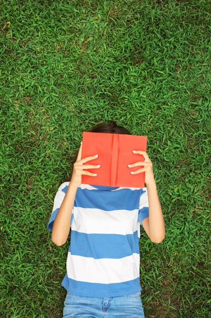 Foto chica adolescente con libro tirado en la hierba verde