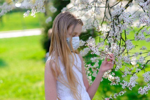 Chica adolescente en máscara médica en jardín floreciente de primavera