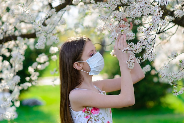 Chica adolescente en máscara médica en jardín floreciente de primavera