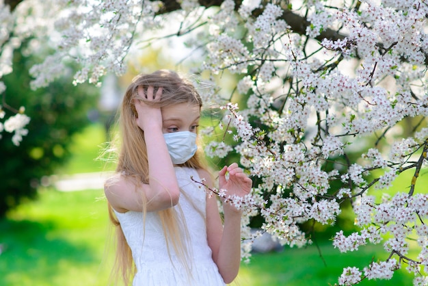Chica adolescente en máscara médica en jardín de flores de primavera. Concepto de distancia social y prevención del coronavirus.