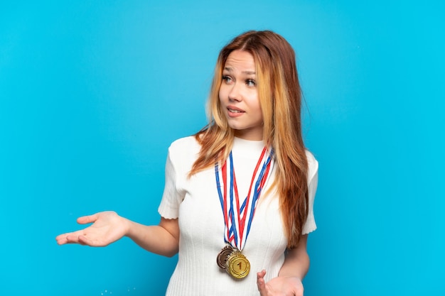 Chica adolescente con medallas sobre antecedentes aislados con expresión de sorpresa mientras mira de lado