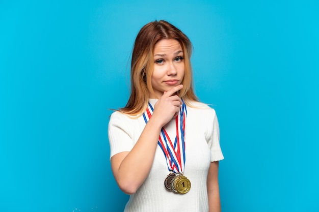 Chica adolescente con medallas sobre fondo aislado pensando