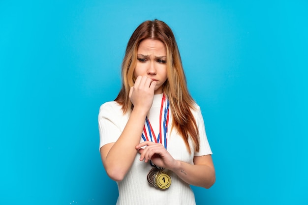 Chica adolescente con medallas sobre pared aislada teniendo dudas