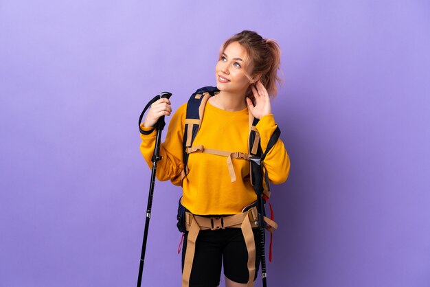 Chica adolescente con mochila y bastones de trekking sobre púrpura aislado pensando en una idea