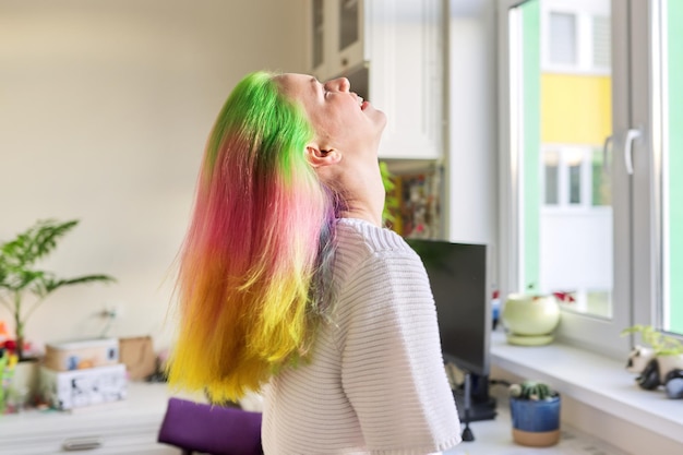 Chica adolescente de moda con cabello largo teñido de arco iris de moda peinándose en casa. Cabello, peinados, coloración moda, juventud y belleza