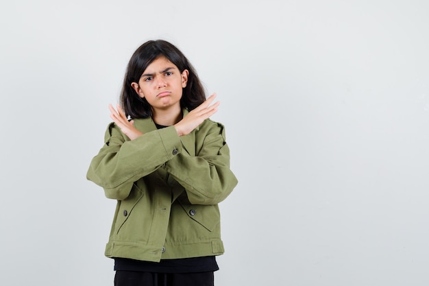 Chica adolescente mostrando gesto de rechazo en camiseta, chaqueta verde y mirando decepcionado, vista frontal.