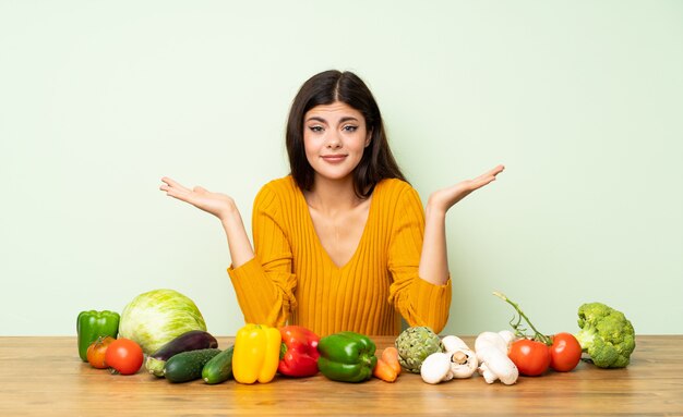 Chica adolescente con muchas verduras teniendo dudas mientras levanta las manos