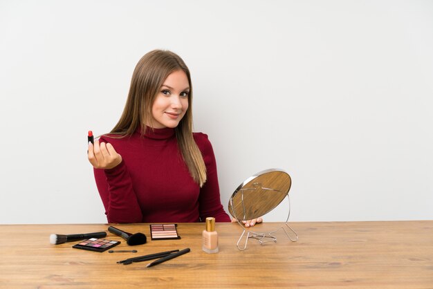 Chica adolescente con paleta de maquillaje y cosméticos en una mesa