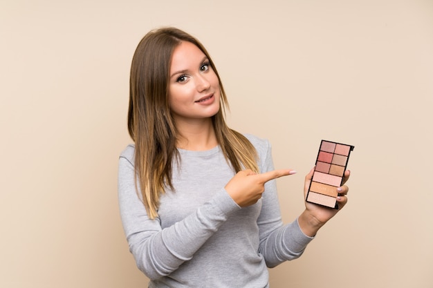 Chica adolescente con paleta de maquillaje sobre aislado y apuntando