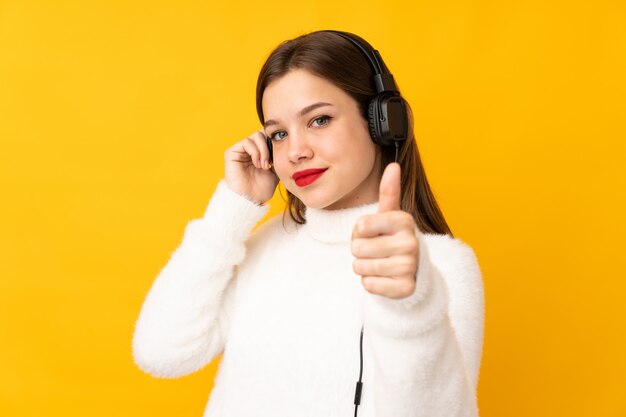 Chica adolescente en la pared amarilla escuchando música y con el pulgar arriba