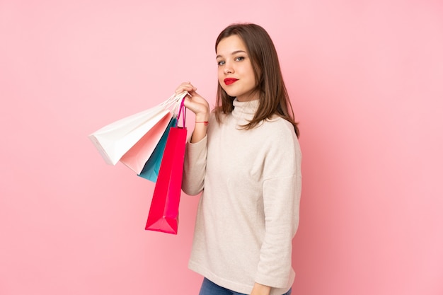 Chica adolescente en pared rosa sosteniendo bolsas de compras y sonriendo