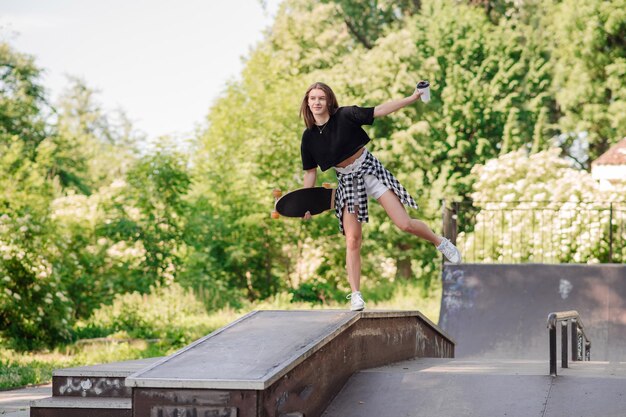 Chica adolescente con una patineta caminando en la rampa en el parque de patinadores