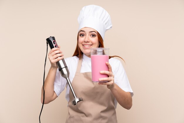 Chica adolescente pelirroja con batidora de mano sobre pared aislada