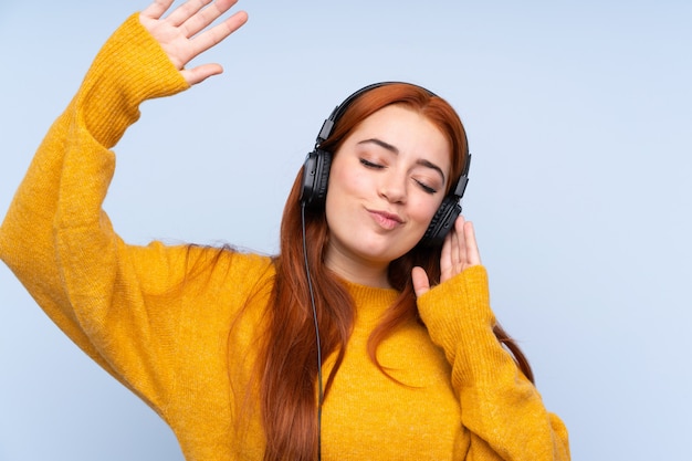 Chica adolescente pelirroja sobre azul escuchando música y bailando