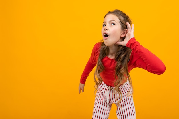 Chica adolescente con pelo rizado en una blusa roja y pantalones a rayas escucha los sonidos sobre un fondo naranja con espacio de copia.