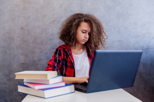 Chica adolescente de pelo rizado websurfing internet en la computadora portátil en casa