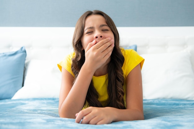 Chica adolescente perezosa cansada bostezando en la cama Niño insomne despierta en la cama y bostezando sintiéndose cansado