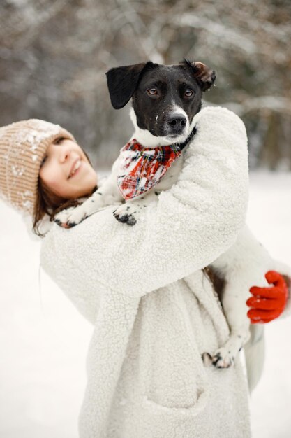 Chica adolescente de pie en el parque de invierno y sosteniendo un perro negro