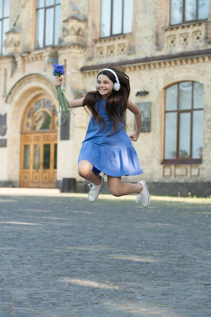 Chica adolescente positiva en auriculares chica salta al aire libre chica despreocupada saltando siente felicidad