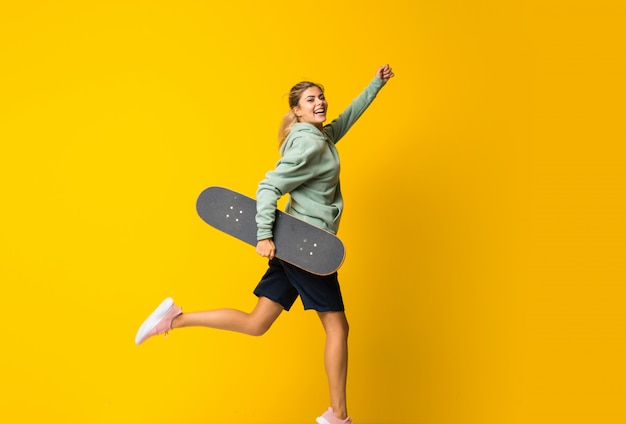 Chica adolescente rubia skater saltando sobre amarillo aislado