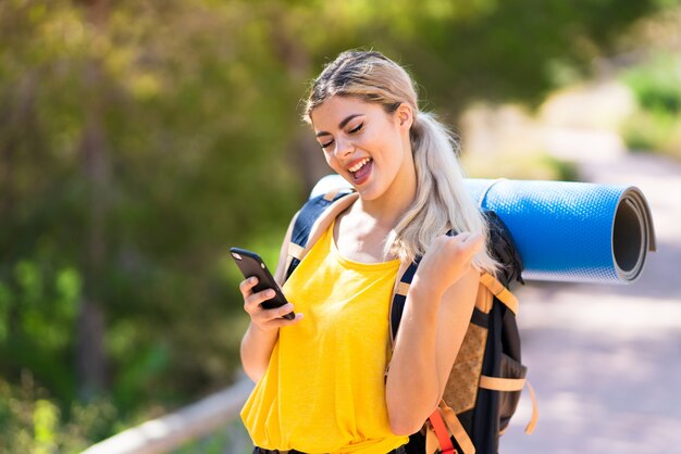 Chica adolescente senderismo al aire libre con teléfono en posición de victoria