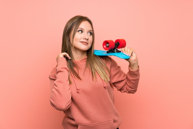 Chica adolescente con skate sobre pared rosa aislado