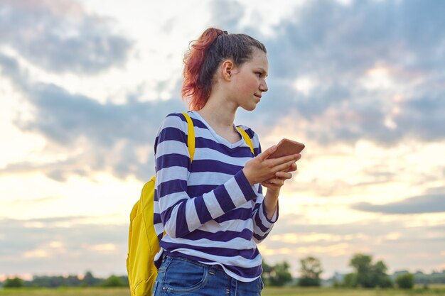 Chica adolescente con smartphone, fondo de prado de naturaleza de cielo.