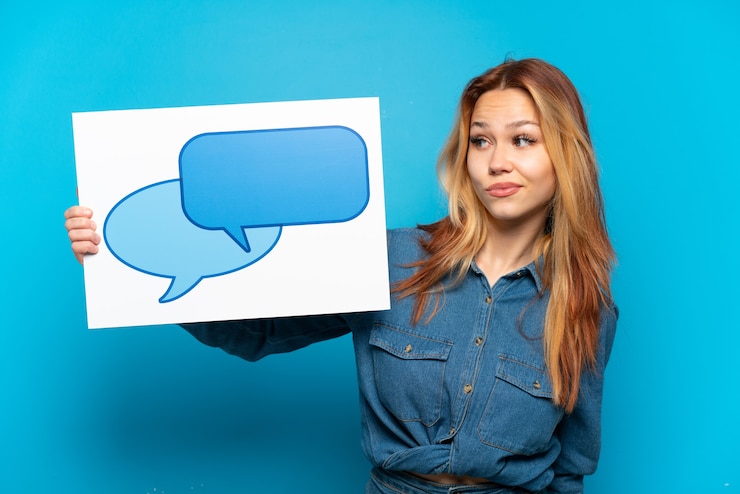 Foto chica adolescente sobre fondo azul aislado sosteniendo un cartel con el icono de la burbuja del discurso