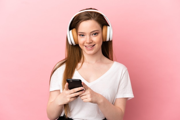 Chica adolescente sobre fondo rosa aislado escuchando música con un móvil y mirando al frente