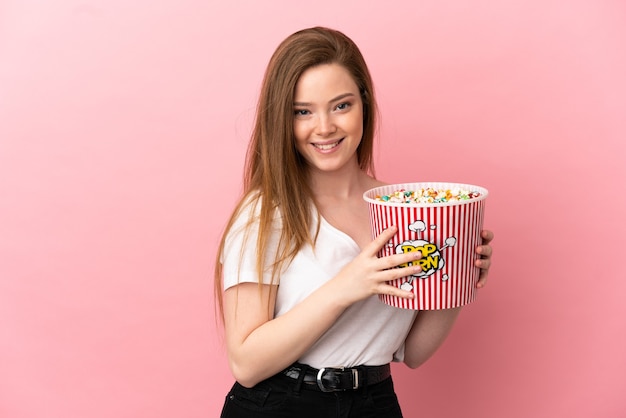 Chica adolescente sobre fondo rosa aislado sosteniendo un gran balde de palomitas de maíz