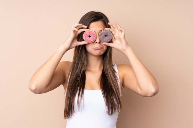 Chica adolescente sobre pared aislada con donas en los ojos con expresión triste