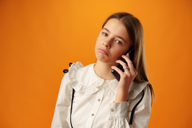 Chica adolescente sobre pared amarilla hablando por teléfono inteligente