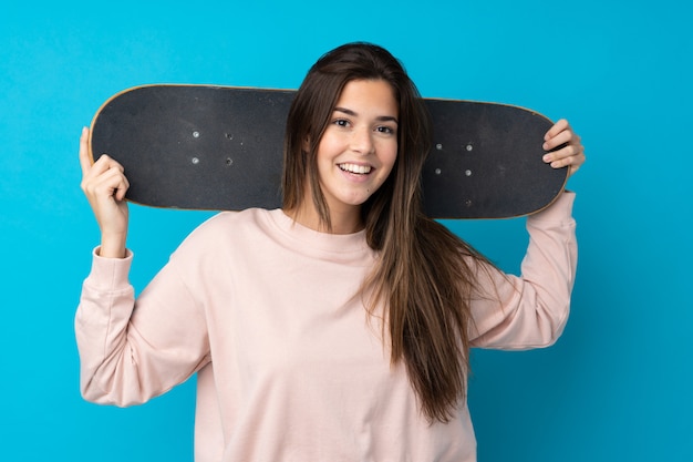 Chica adolescente sobre pared azul aislada con un patín con expresión feliz