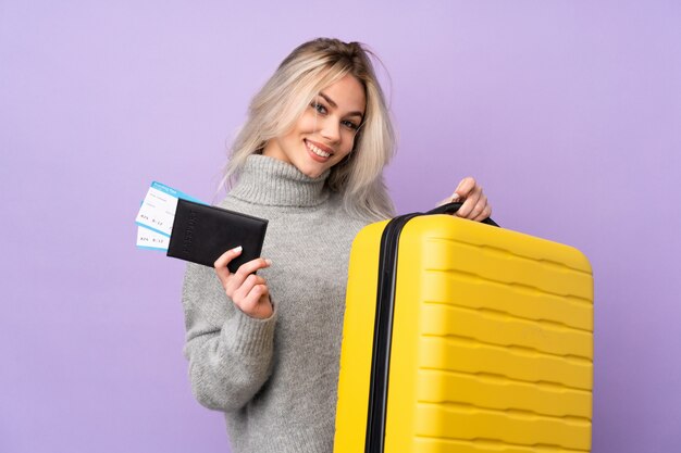 Chica adolescente sobre púrpura aislado en vacaciones con maleta y pasaporte