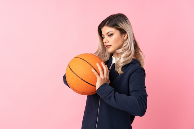 Chica adolescente sobre rosa aislado con pelota de baloncesto