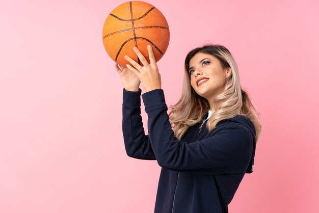 Chica adolescente sobre rosa aislado con pelota de baloncesto