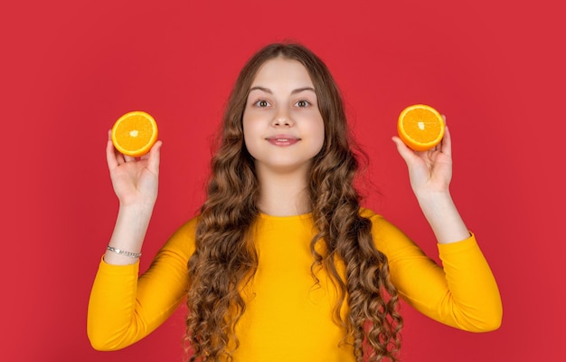 Una chica adolescente sonríe sosteniendo una fruta de naranja sobre un fondo púrpura