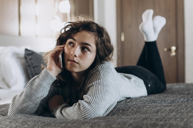 Chica adolescente sonriente feliz hablando por teléfono acostado en la cama