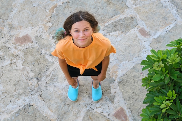 Chica adolescente sonriente mirando hacia arriba, vista superior, mujer de pie sobre la acera de piedra gris