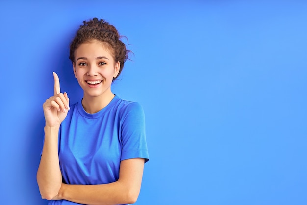 Chica adolescente sonriente positiva apuntando con el dedo hacia arriba.