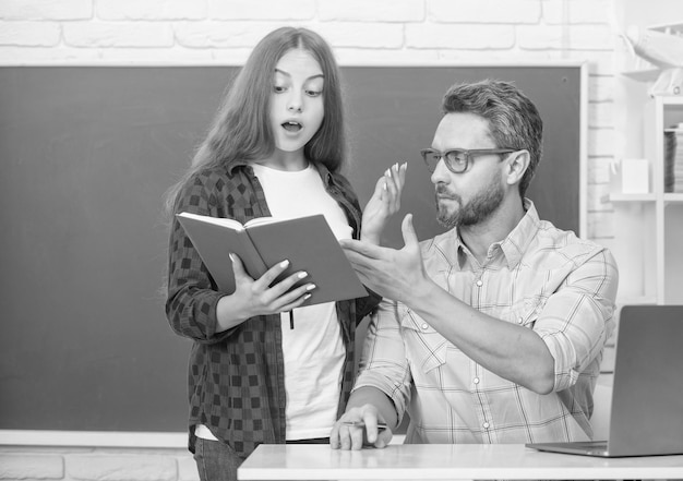 Chica adolescente sorprendida y profesor en la escuela secundaria con libro de trabajo en la educación de pizarra