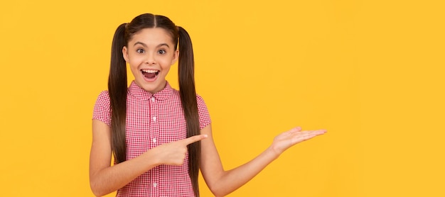 Chica adolescente sorprendida señalando con el dedo sobre fondo amarillo copia espacio anuncio Cara de niño cartel horizontal adolescente chica aislada retrato banner con espacio de copia