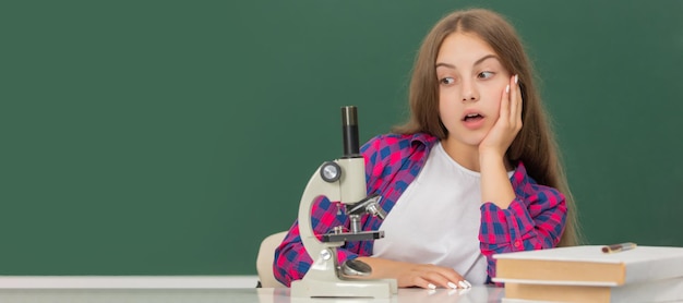 Chica adolescente sorprendida usando microscopio en la escuela secundaria en pizarra