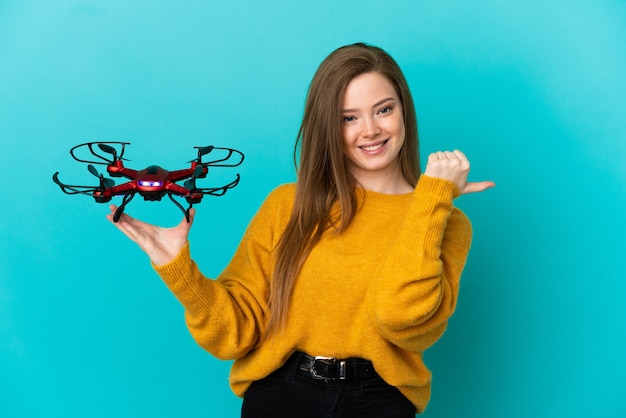 Chica adolescente sosteniendo un avión no tripulado sobre fondo azul aislado apuntando hacia el lado para presentar un producto