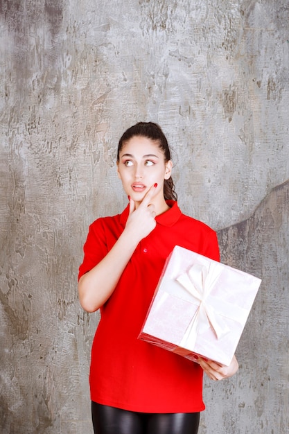 Foto chica adolescente sosteniendo una caja de regalo rosa envuelta con cinta blanca y parece pensativa.