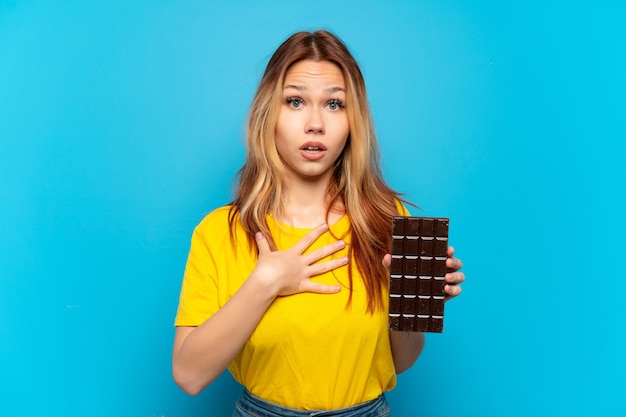 Chica adolescente sosteniendo chocolat sobre fondo azul aislado sorprendido y conmocionado mientras mira a la derecha